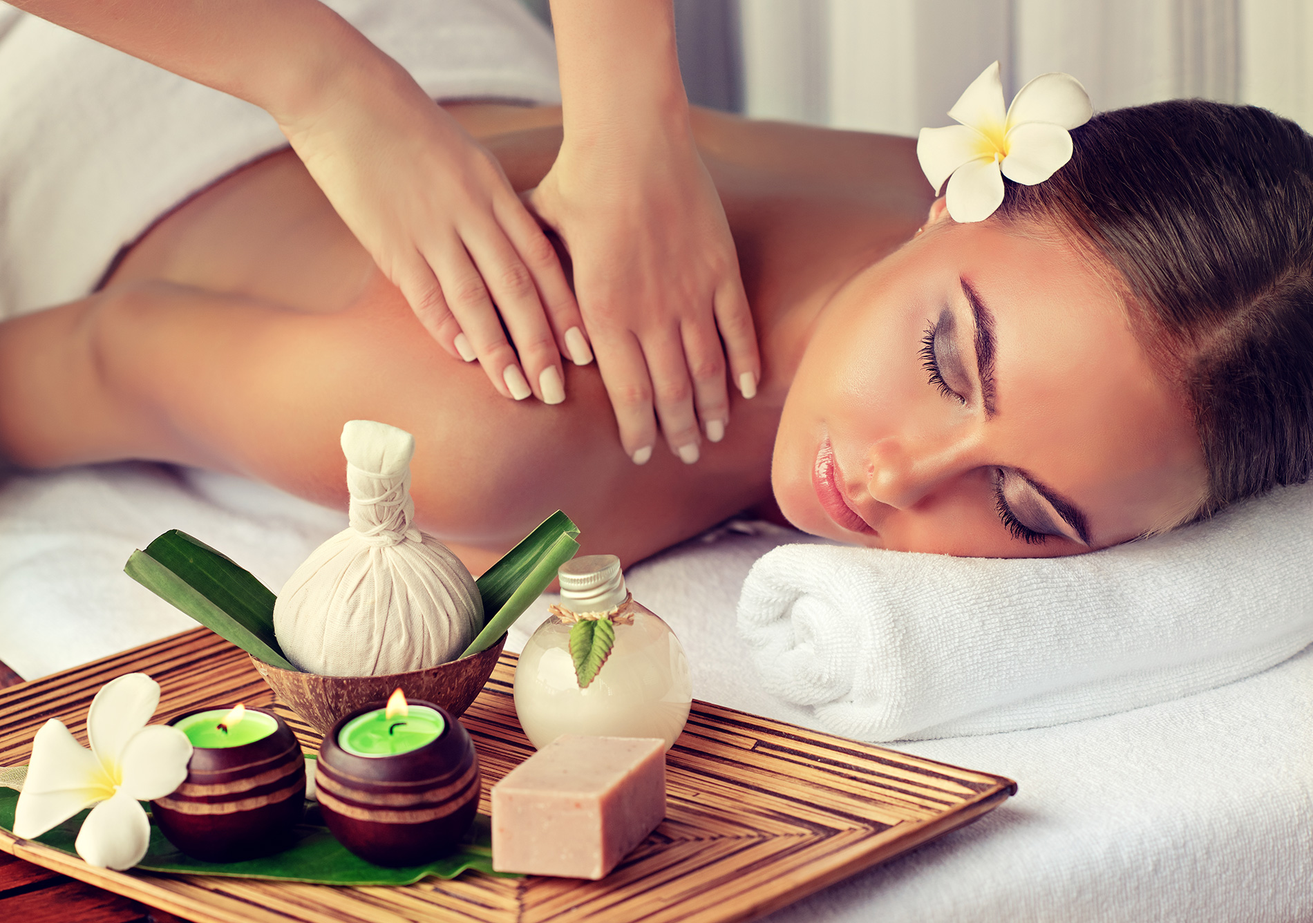 Femme au spa reçoit un massage relaxant avec une fleur de tiaré dans les cheveux